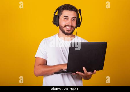 Joyeux brésilien latino-américain tenant un ordinateur portable et souriant, avec micro-casque, concept de travailleur de télémarketing Banque D'Images