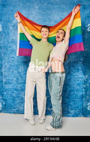 Une communauté homosexuelle pleine d'enthousiasme avec des vêtements décontractés portant le drapeau lgbt tout en célébrant le mois de la fierté et en se tenant ensemble sur un baba bleu marbré Banque D'Images