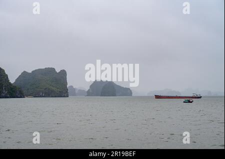 Un vieux navire rouillé et un petit bateau de pêche en mer parmi les îles calcaires de Bai Tu long Bay, Halong Bay, Vietnam. Banque D'Images