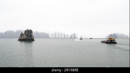 Barges naviguant parmi les îles et îlots calcaires caractéristiques s'évanouissant dans la brume à Bai Tu long Bay, Halong Bay, Vietnam. Banque D'Images