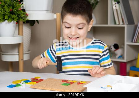 Un enfant d'âge préscolaire joue avec une mosaïque, construit des figures sur une planche, martelant des ongles avec un marteau sur des parties multicolores du concepteur Banque D'Images