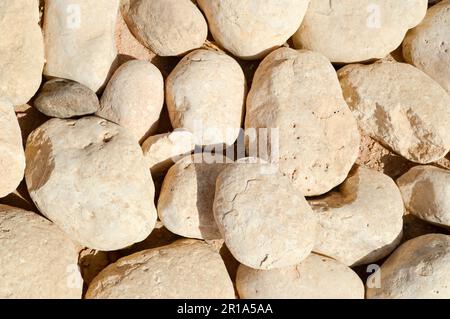Texture d'un mur en pierre, routes de grandes pierres rondes et ovales avec sable avec des coutures de couleur jaune foncé brun noir. L'arrière-plan. Banque D'Images