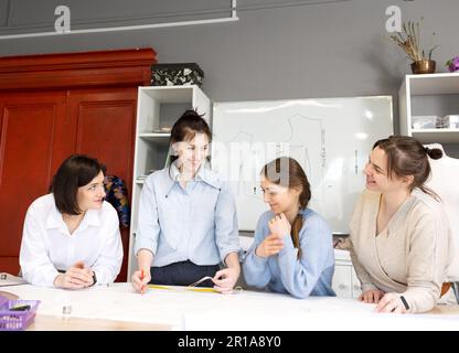 Quatre stylistes féminins travaillent ensemble dans un studio de couture. Un groupe de femmes couturiers discute de tissu, de modèle et de croquis dans une couture des œuvres Banque D'Images