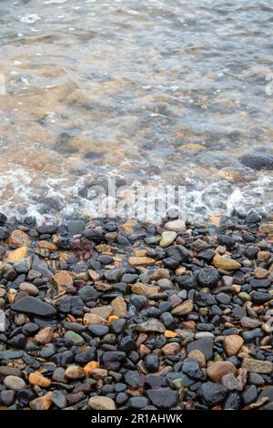 Pierres sur une plage noire en Islande avec des éclaboussures d'eau Banque D'Images