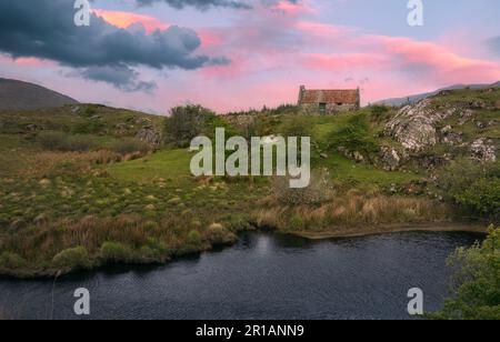 Magnifique paysage de lever de soleil avec vieux cottage en étain rouillé sur le toit au bord de la rivière avec des montagnes en arrière-plan au parc national du Connemara dans le comté de Galway, en Irlande Banque D'Images