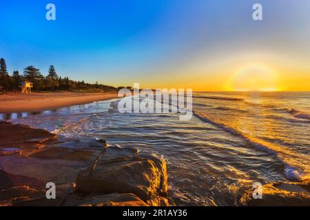 Soleil haut en couleur sur l'horizon de l'océan Pacifique au large de la plage de sable des Caves en Australie. Banque D'Images