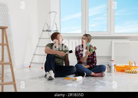 Couple heureux avec des brosses et des outils de peinture sur le sol dans l'appartement pendant la réparation Banque D'Images