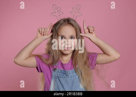 Une jeune fille joueuse portant un magnifique serre-tête sur fond rose Banque D'Images