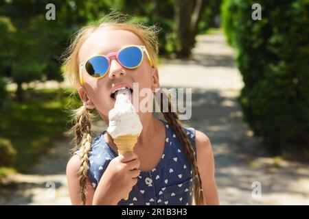 Adorable petite fille mangeant une délicieuse glace à l'extérieur le jour ensoleillé de l'été, espace pour le texte Banque D'Images