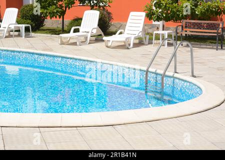 Piscine extérieure avec mains courantes et chaises longues vides à l'hôtel, le jour du soleil Banque D'Images