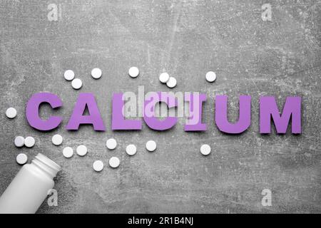 Word calcium fait de lettres en papier violet, bouteille médicale et pilules sur fond gris, vue de dessus Banque D'Images