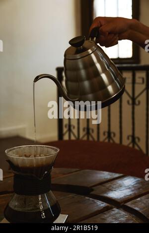 Barista verse de l'eau de la bouilloire dans la tasse avec du café et un égouttoir à vagues dans le café, en gros plan Banque D'Images