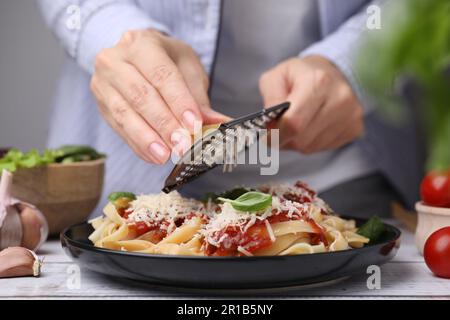 Femme râpant du parmesan sur de délicieuses pâtes à table en bois, en gros plan Banque D'Images