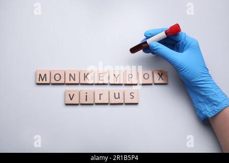 Infirmière tenant le tube à essai et les mots Monkeypox virus fait de cubes en bois sur fond blanc, vue de dessus Banque D'Images