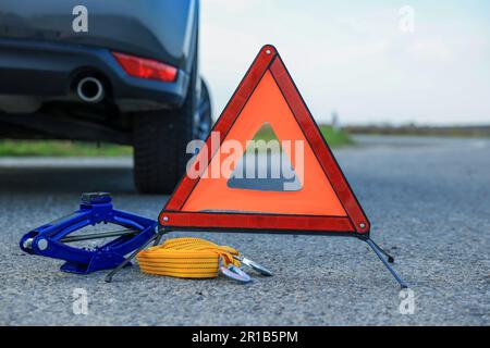 Triangle d'avertissement d'urgence, sangle de remorquage et cric articulé près de la voiture à l'extérieur. Équipement de sécurité Banque D'Images