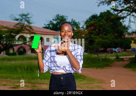 Jeune heureuse belle femme africaine montre téléphone avec affichage vert en admirant de nouveaux achats en ligne Banque D'Images