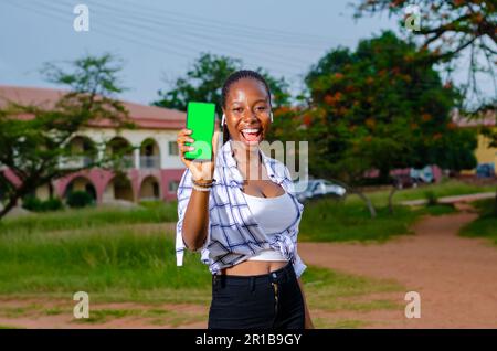 Jeune heureuse belle femme africaine montre téléphone avec affichage vert en admirant de nouveaux achats en ligne Banque D'Images