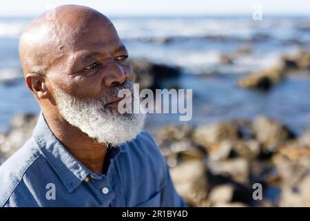 Homme afro-américain expérimenté et attentionné, assis sur des rochers et admirant la vue sur le bord de mer Banque D'Images