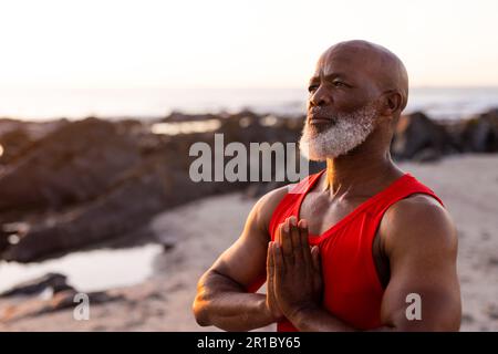 Homme afro-américain senior concentré pratiquant le yoga et faisant la pose à la plage Banque D'Images