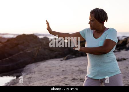 Femme afro-américaine senior concentrée pratiquant le yoga et faisant la pose à la plage Banque D'Images