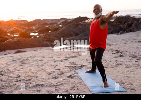 Homme afro-américain senior concentré pratiquant le yoga et faisant la pose à la plage Banque D'Images