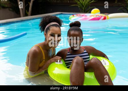Portrait de la mère et de la fille afro-américaines sur gonflable dans la piscine Banque D'Images