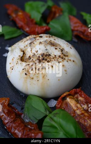 Burrata, un fromage au lait de vache italien à base de mozzarella, de Stracciatella et de crème de Puglia, en Italie, servi avec du sel, du poivre, des tomates séchées et Banque D'Images