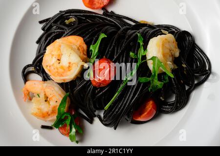 Spaghetti al Nero di Seppia con Gamberi, pâtes italiennes à l'encre de calmar, crevettes, tomates et rocola Banque D'Images