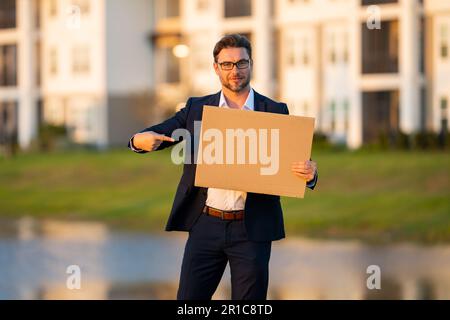 Beau homme d'affaires tenant le tableau vide et pointant le doigt. Homme montrant un panneau vierge avec espace de copie. Idée et offre. Votre publicité. Vide a Banque D'Images