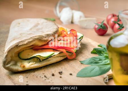 Cuisine italienne, pizza calzone fermée sur fond de bois rustique. Rempli de poivrons et de courgettes. Sur fond flou petit tomatoe rouge , mozzarella Banque D'Images