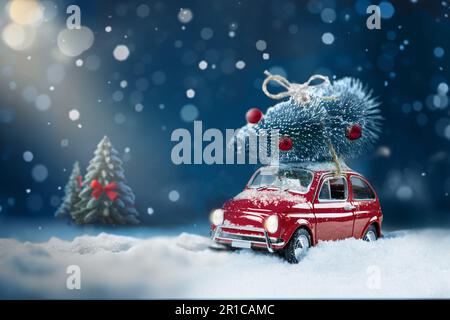 Voiture rouge rétro transportant l'arbre de noël sur le toit dans la forêt hivernale enneigée de nuit. Arrière-plan de Noël. Copier l'espace. Banque D'Images