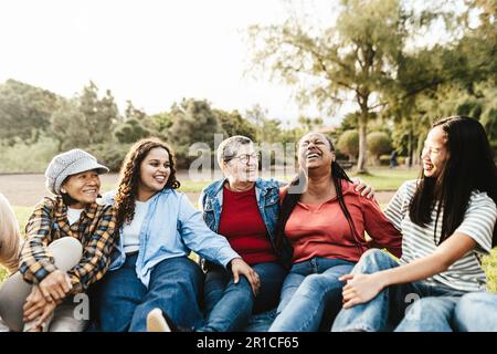 Groupe de femmes heureux de plusieurs générations avec différentes ethnies ayant le plaisir assis sur l'herbe dans un parc public - concept d'autonomisation des femmes Banque D'Images