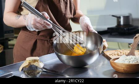 Une femme fouette des œufs avec un fouet dans un grand bol en métal de la cuisine. Banque D'Images