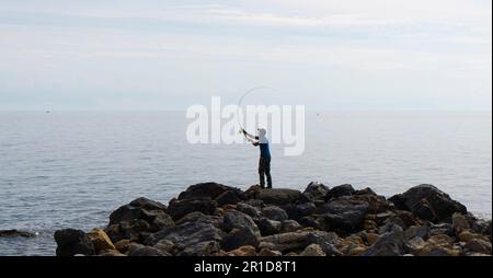 Un pêcheur solitaire se tient sur les rives de la mer Égée jette sa ligne dans l'espoir de pêcher un poisson Banque D'Images