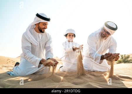 Famille de trois générations effectuant un safari dans le désert de Dubaï portant une tenue de kandura blanche. Grand-père, fils et petits-fils passent du temps ensemble dans t Banque D'Images