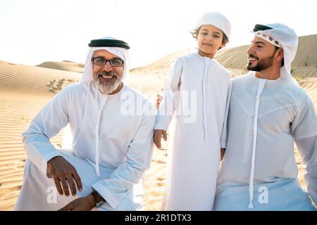 Famille de trois générations effectuant un safari dans le désert de Dubaï portant une tenue de kandura blanche. Grand-père, fils et petits-fils passent du temps ensemble dans t Banque D'Images