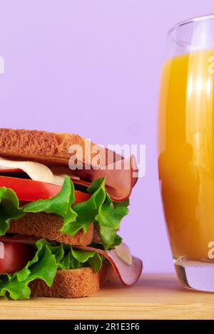 Délicieux sandwich au jambon avec salade fraîche et cornichon servi sur un plateau en bois. Avec un verre de jus d'orange. Banque D'Images