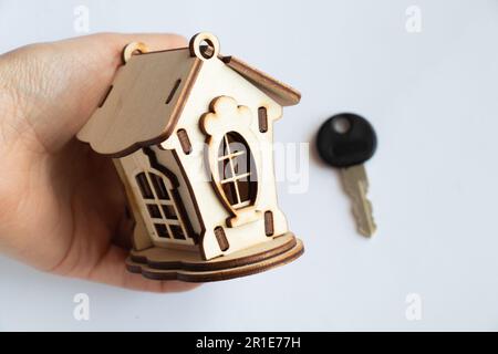 une petite maison de jouets en bois tient une main de femme sur un fond blanc Banque D'Images