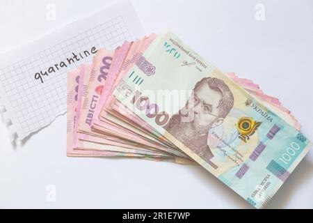 Un paquet de hryvnia ukrainien et le mot quarantaine en anglais est écrit sur un morceau de papier sur un blanc Banque D'Images