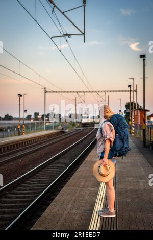 Femme voyageur attendant à la gare pendant le coucher du soleil. Le touriste solo est prêt pour un voyage d'été Banque D'Images
