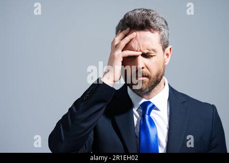 Homme d'affaires stressé en costume ayant mal de tête. Un homme d'affaires fatigué fait des heures supplémentaires et a des maux de tête. L'homme surtravaillé souffre de maux de tête. Migraine Banque D'Images