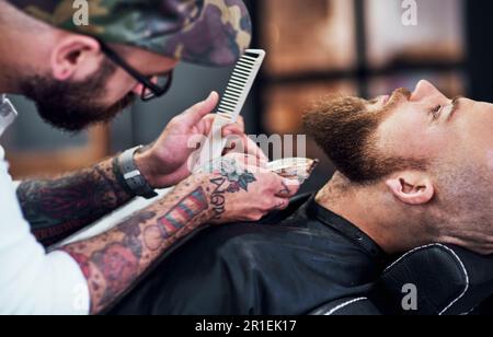 Il me fait confiance avec sa barbe. un beau jeune homme qui tond sa barbe et l'alignera dans un salon de coiffure. Banque D'Images