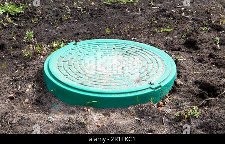 Nouveau trou d'homme en métal vert sur le terrain. Travaux de réparation. Le toit ouvrant fermé ne présente pas de danger pour les piétons et les véhicules. Réparation de canalisations souterraines Banque D'Images