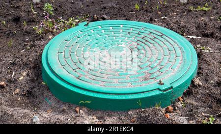 Nouveau trou d'homme en métal vert sur le terrain. Travaux de réparation. Le toit ouvrant fermé ne présente pas de danger pour les piétons et les véhicules. Réparation de canalisations souterraines Banque D'Images