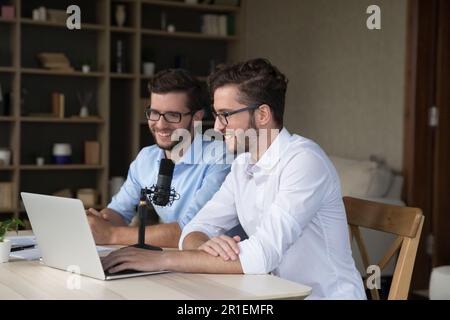 Joyeux twin hommes assis à un ordinateur portable et un microphone studio Banque D'Images