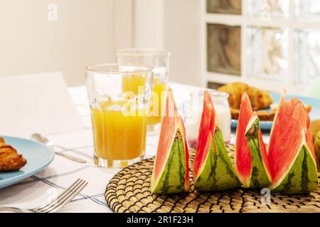 Une table à manger avec un petit déjeuner avec beaucoup de fruits, jus d'orange frais et une nappe blanche Banque D'Images