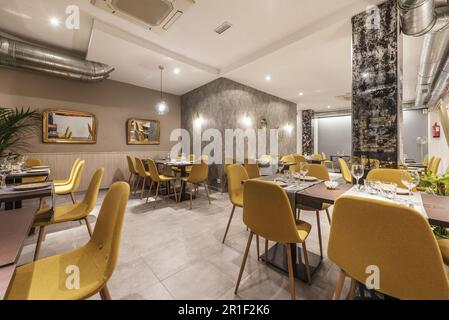 salle à manger d'un restaurant avec des tables en bois, des chaises rembourrées jaunes et des miroirs encadrés d'or sur le mur Banque D'Images