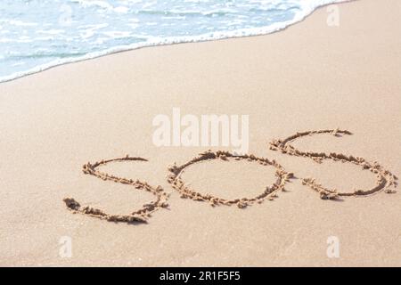 Message SOS dessiné sur la plage de sable près de la mer Banque D'Images