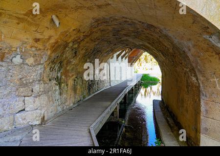 Promenade dans le passage voûté sous le pont en pierre enjambant la rivière Loing dans la ville médiévale de Moret-sur-Loing en Seine et Marne, France Banque D'Images