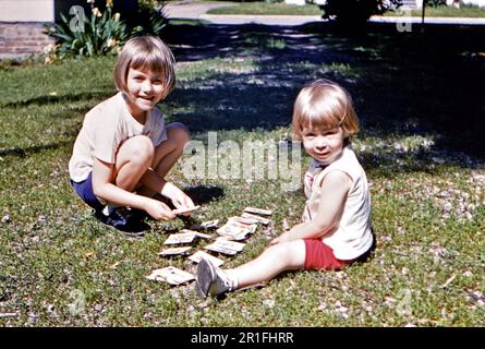 Deux jeunes enfants jouant avec un jeu de cartes dans une cour ca. 1961 Banque D'Images